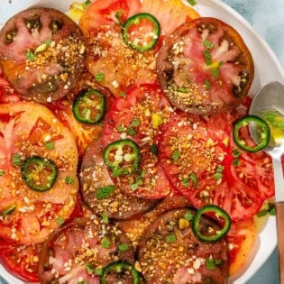 Heirloom tomato salad topped with dukkah and mint on a platter with a spoon next to a cup of the dressing and a small bowl of dukkah.