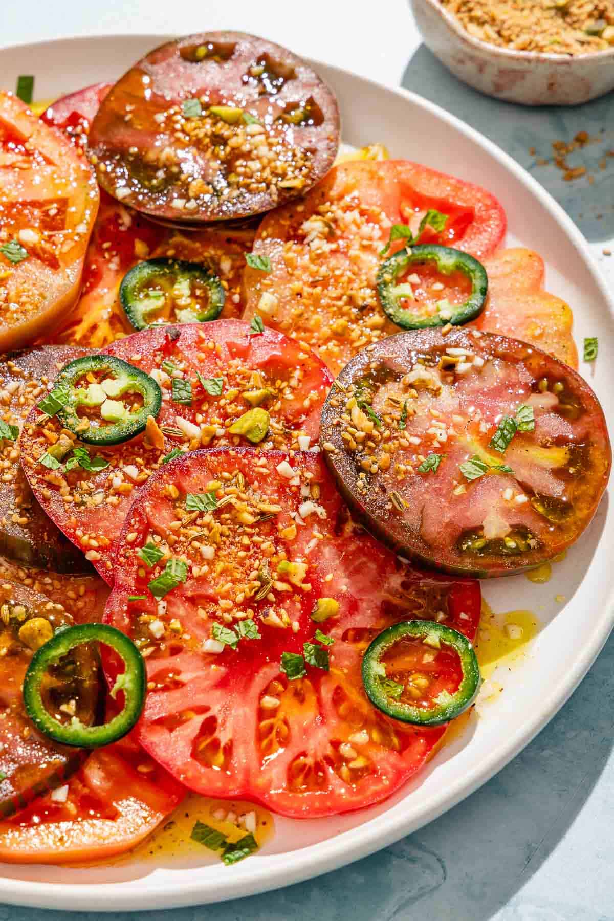 Heirloom tomato salad topped with dukkah and mint on a platter next to a small bowl of dukkah.