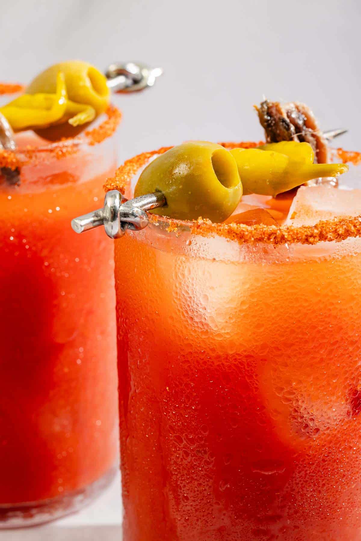 A close up of a Mediterranean bloody Mary garnished with skewer of an olive, pickled pepper and anchovy.