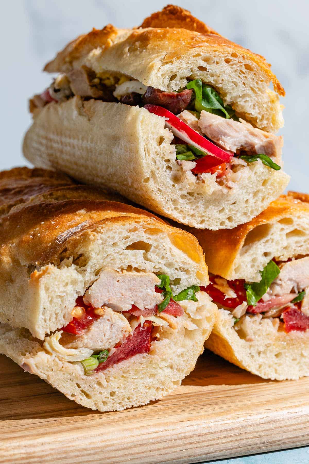 A stack of 3 pan bagnats on a wooden cutting board.