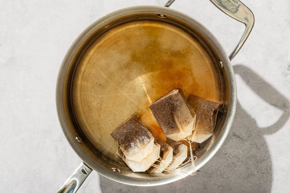 Several tea bags in water in a saucepan.