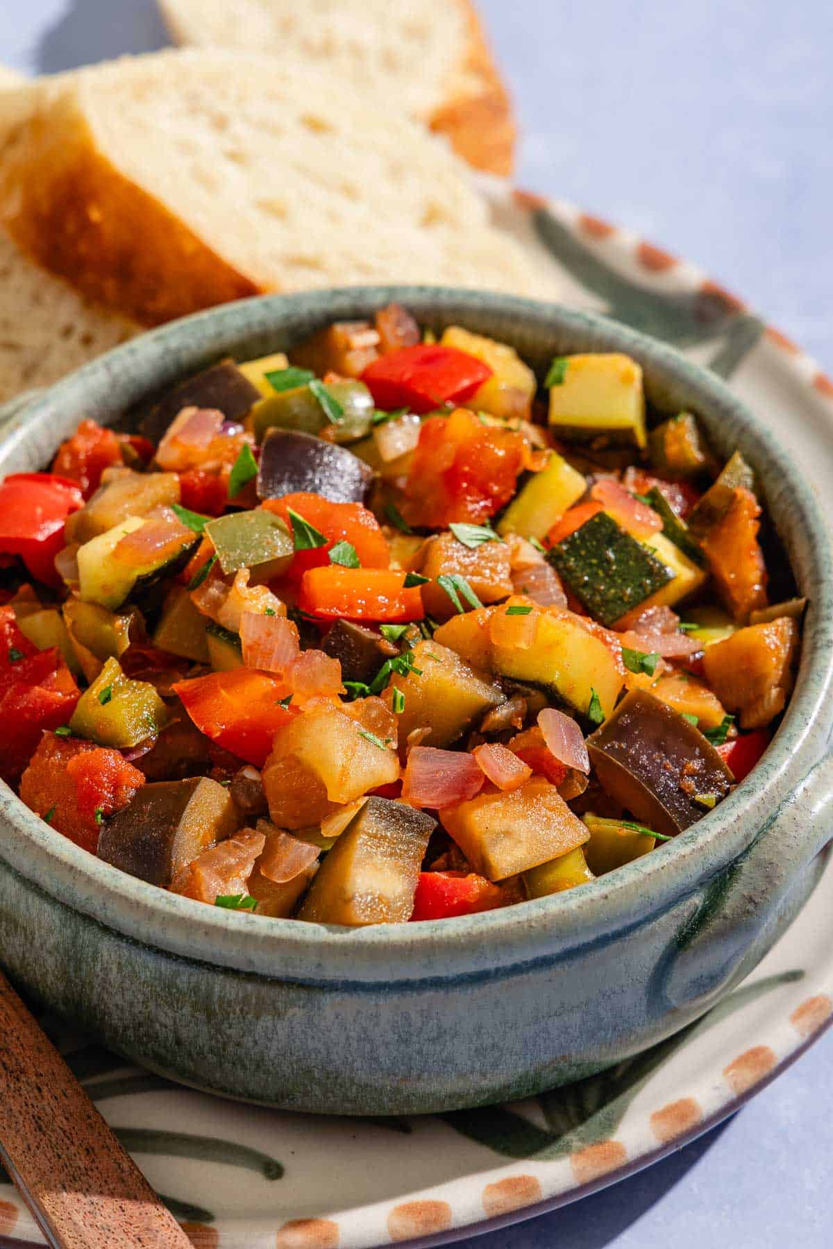 Spanish pisto in a bowl on a plate with slices of crusty bread.