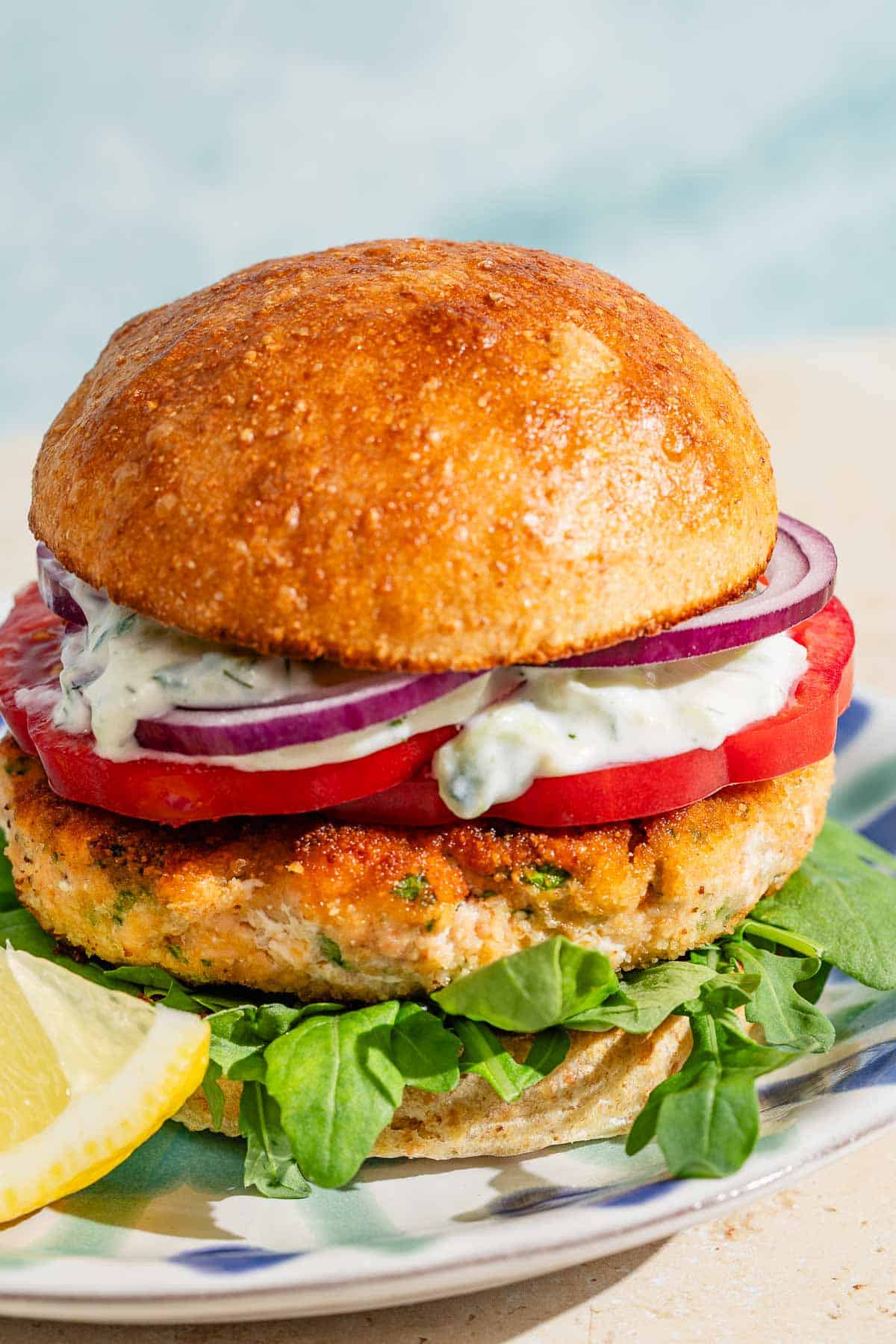 A close up of a salmon burger on a plate with a lemon wedge.