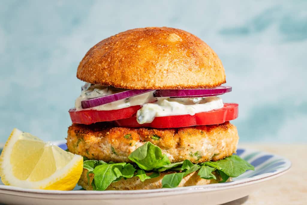 A salmon burger on a plate with a lemon wedge.