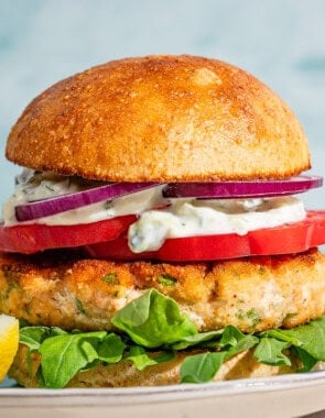 A salmon burger on a plate with a lemon wedge.