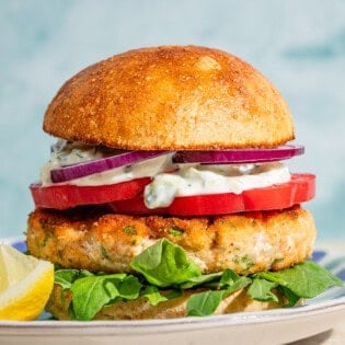 A salmon burger on a plate with a lemon wedge.
