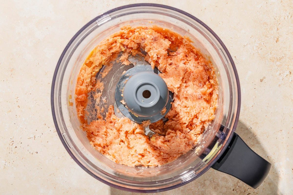 Ground salmon in the bowl of a food processor fitted with a blade.