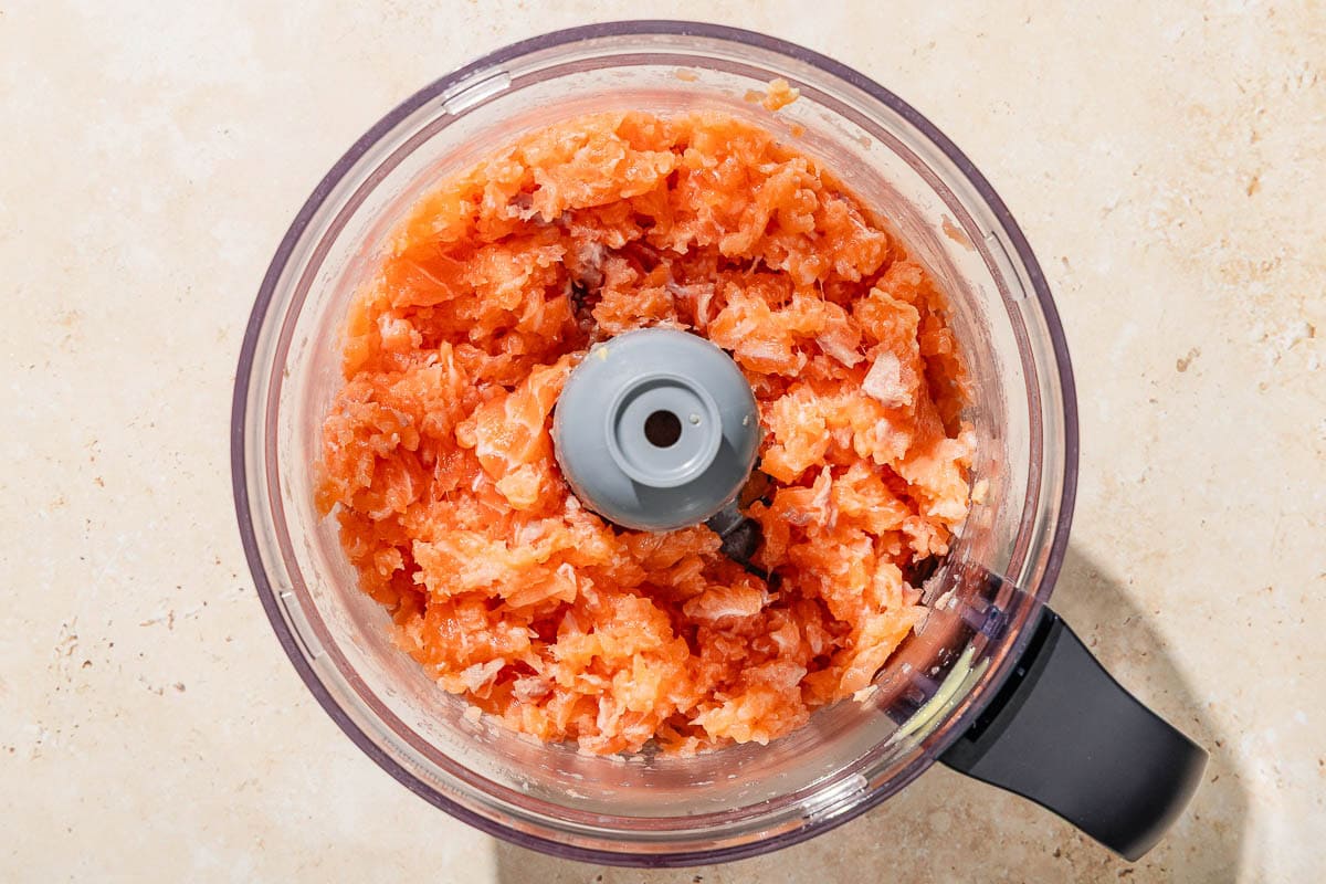 Ground salmon in the bowl of a food processor fitted with a blade.