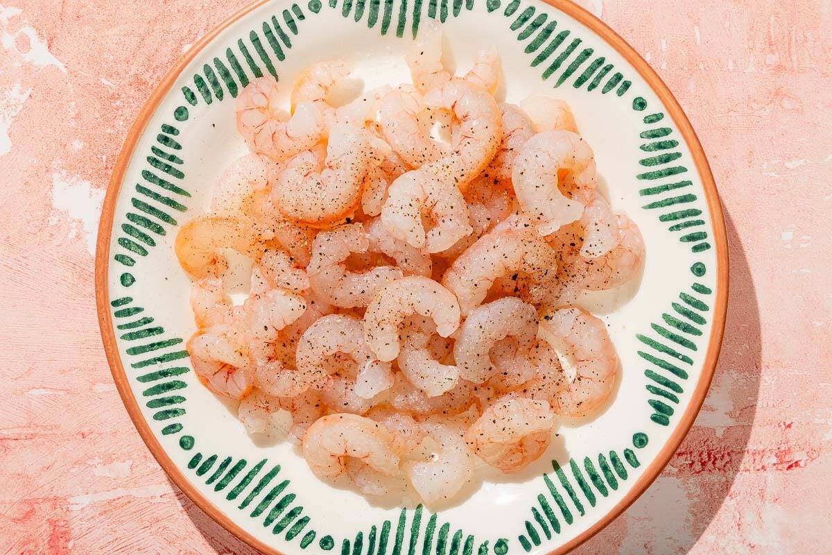 Raw shrimp seasoned with salt and pepper on a plate.