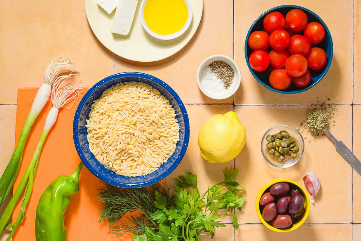 Ingredients for orzo salad including orzo, cherry tomatoes, green onions, green bell pepper, parsley, fresh dill, kalamata olives, capers, feta cheese, lemon, olive oil, garlic, dried oregano, salt, and black pepper.