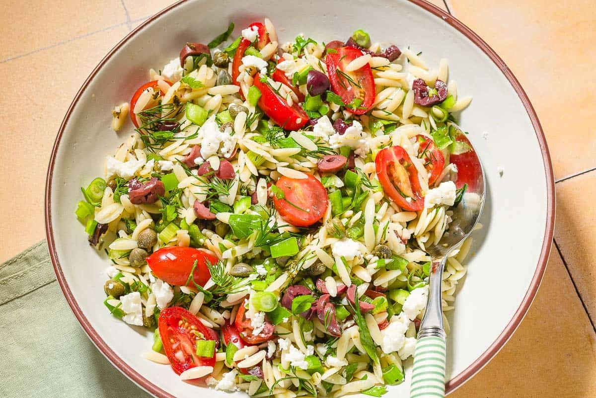 Orzo salad in a bowl with a spoon.