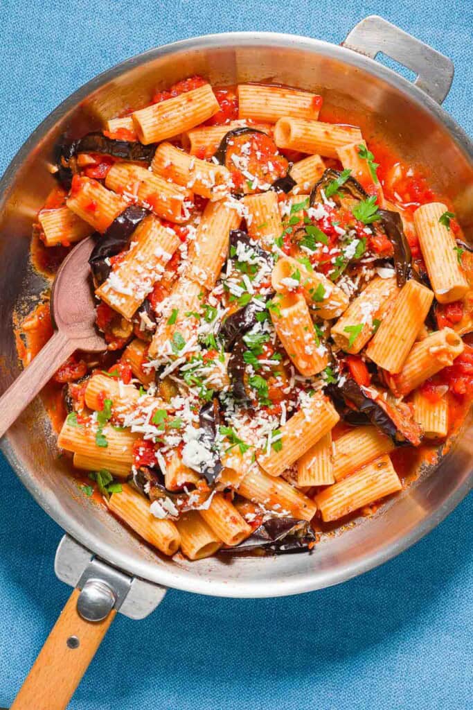 Pasta alla norma in a skillet with a wooden spoon.