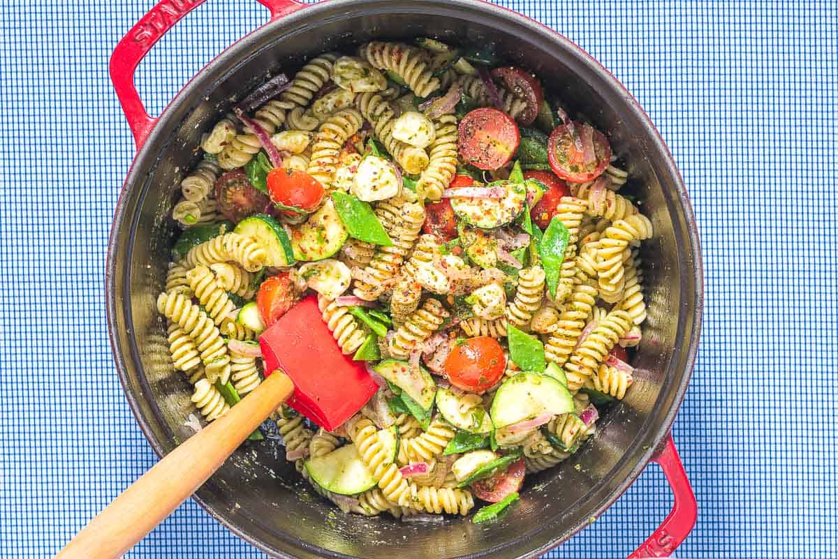 The pesto pasta salad being stirred together in a dutch oven with a spatula.