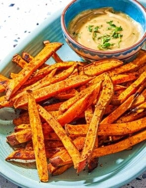 Sweet potato fries on a platter with a bowl of tahini sauce.