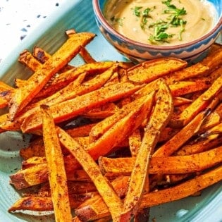Sweet potato fries on a platter with a bowl of tahini sauce.