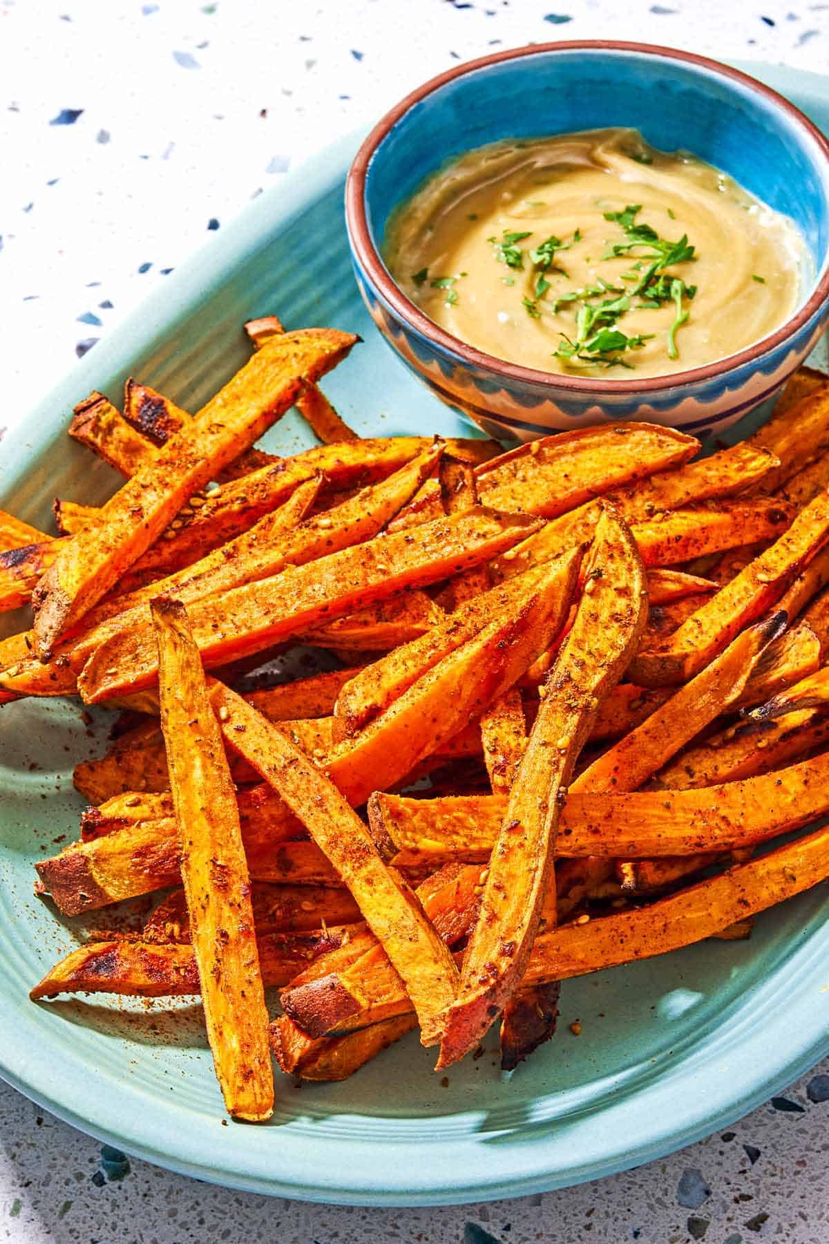 Sweet potato fries on a platter with a bowl of tahini sauce.