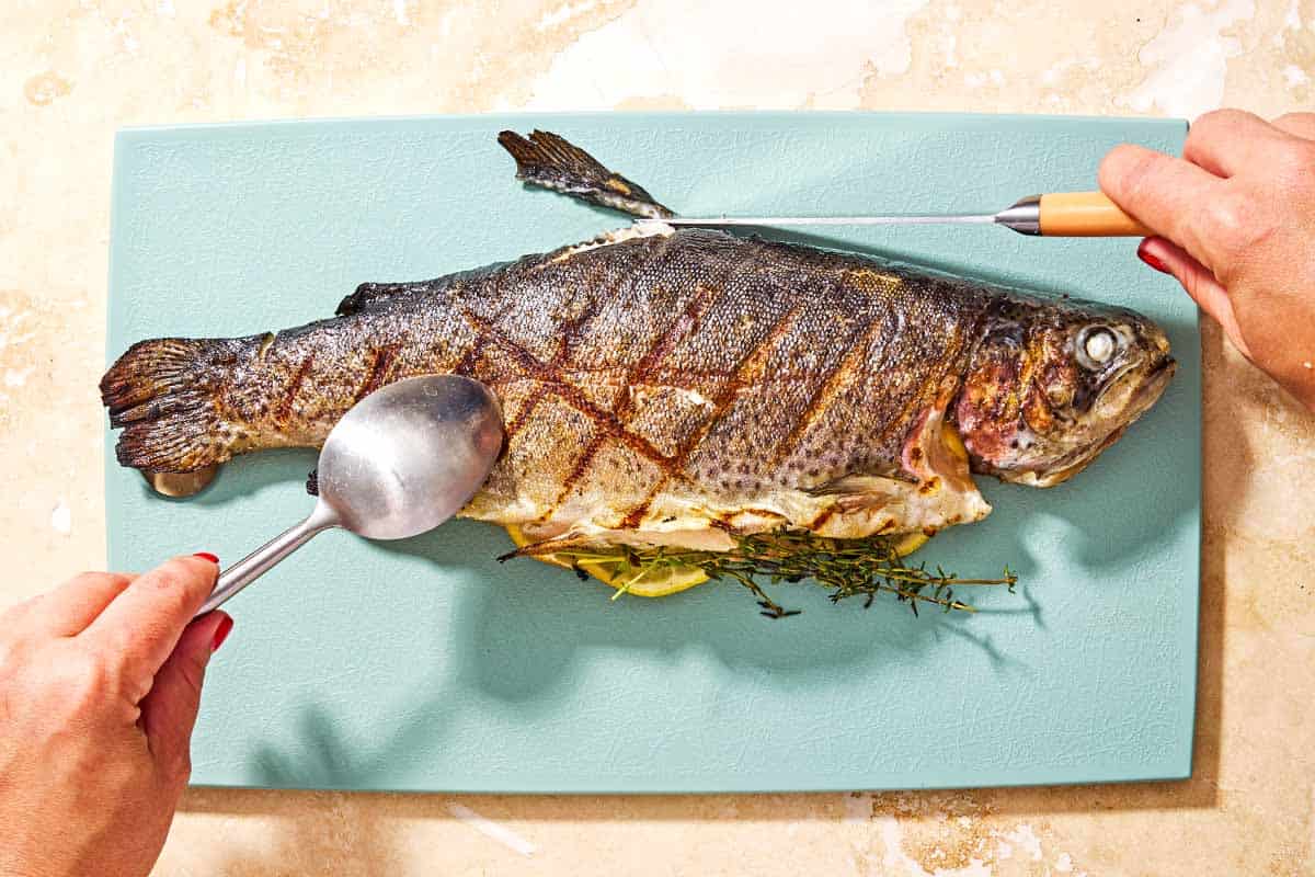 A whole grilled trout being filleted on a cutting board.
