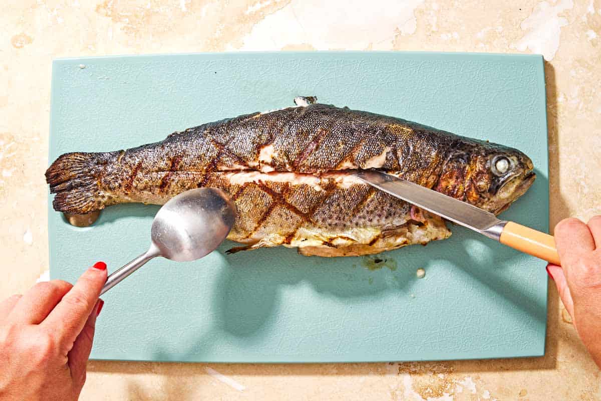 A whole grilled trout being filleted on a cutting board.