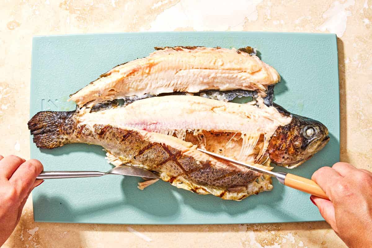 A whole grilled trout being filleted on a cutting board.
