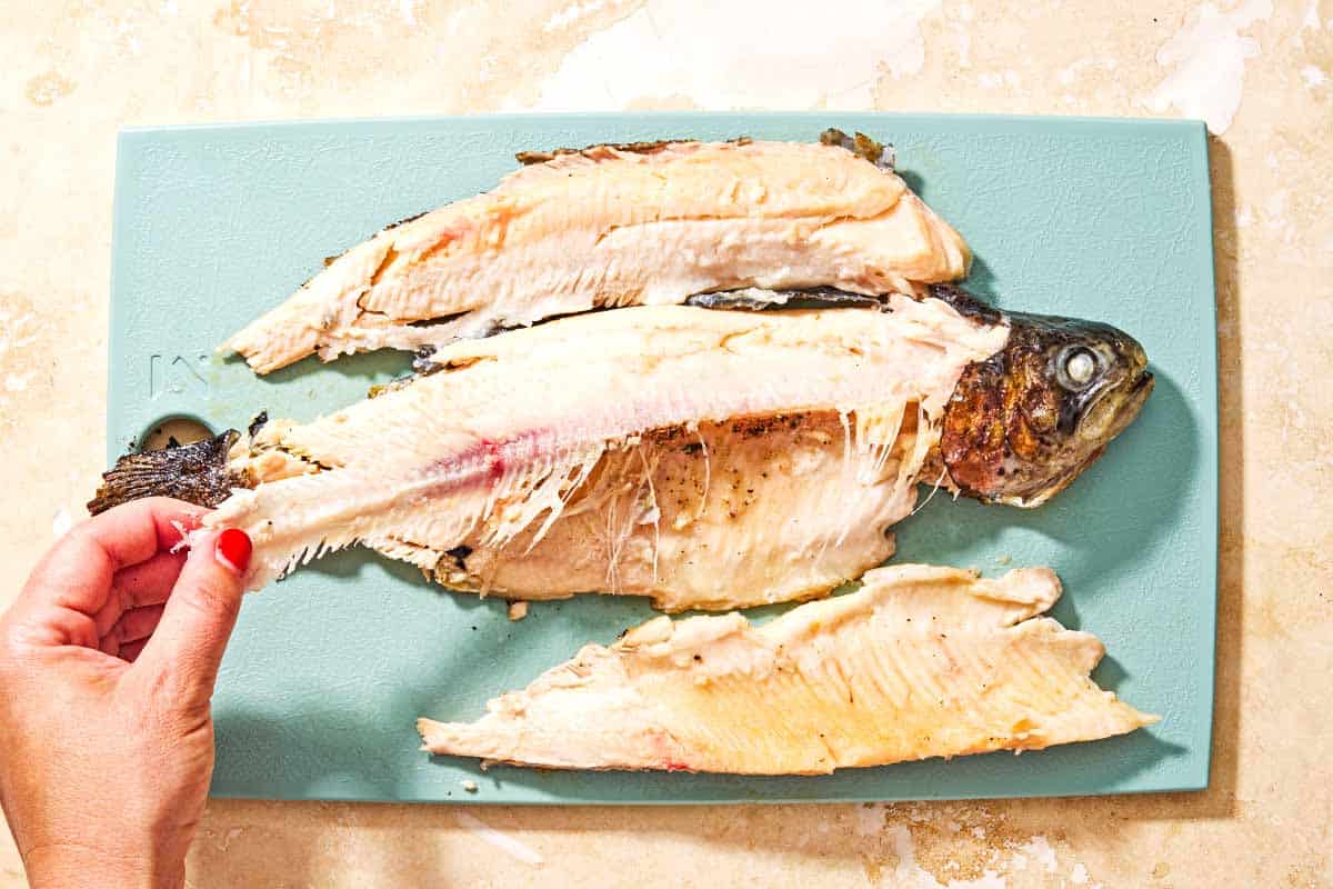 A whole grilled trout being filleted on a cutting board.