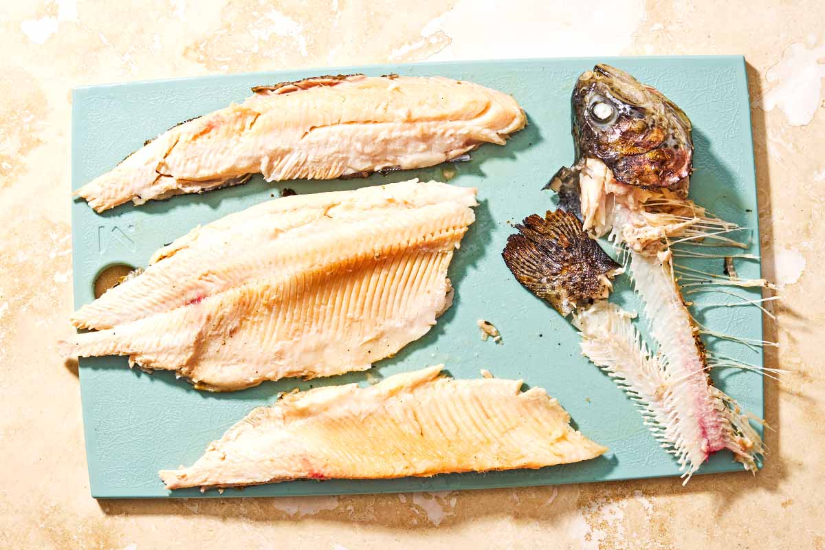 The grilled trout fillets on a cutting board next to the bones of the fish.