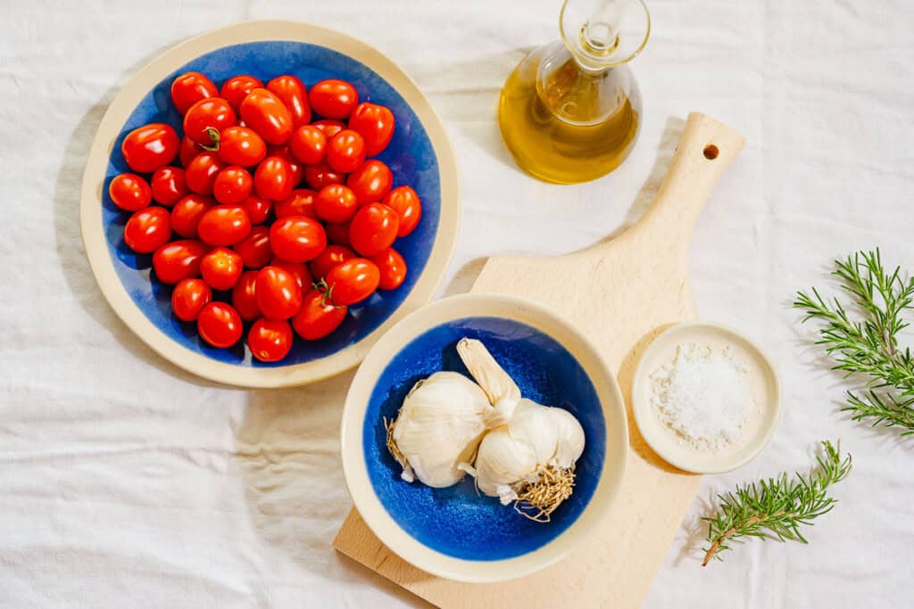 Ingredients for tomato confit including cherry tomatoes, olive oil, garlic rosemary and kosher salt.
