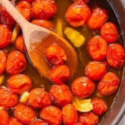 The ingredients for the tomato confit cooking and being stirred together in a saucepan with a wooden spoon.