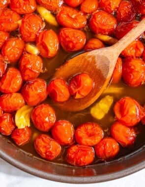 The ingredients for the tomato confit cooking and being stirred together in a saucepan with a wooden spoon.