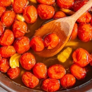 The ingredients for the tomato confit cooking and being stirred together in a saucepan with a wooden spoon.