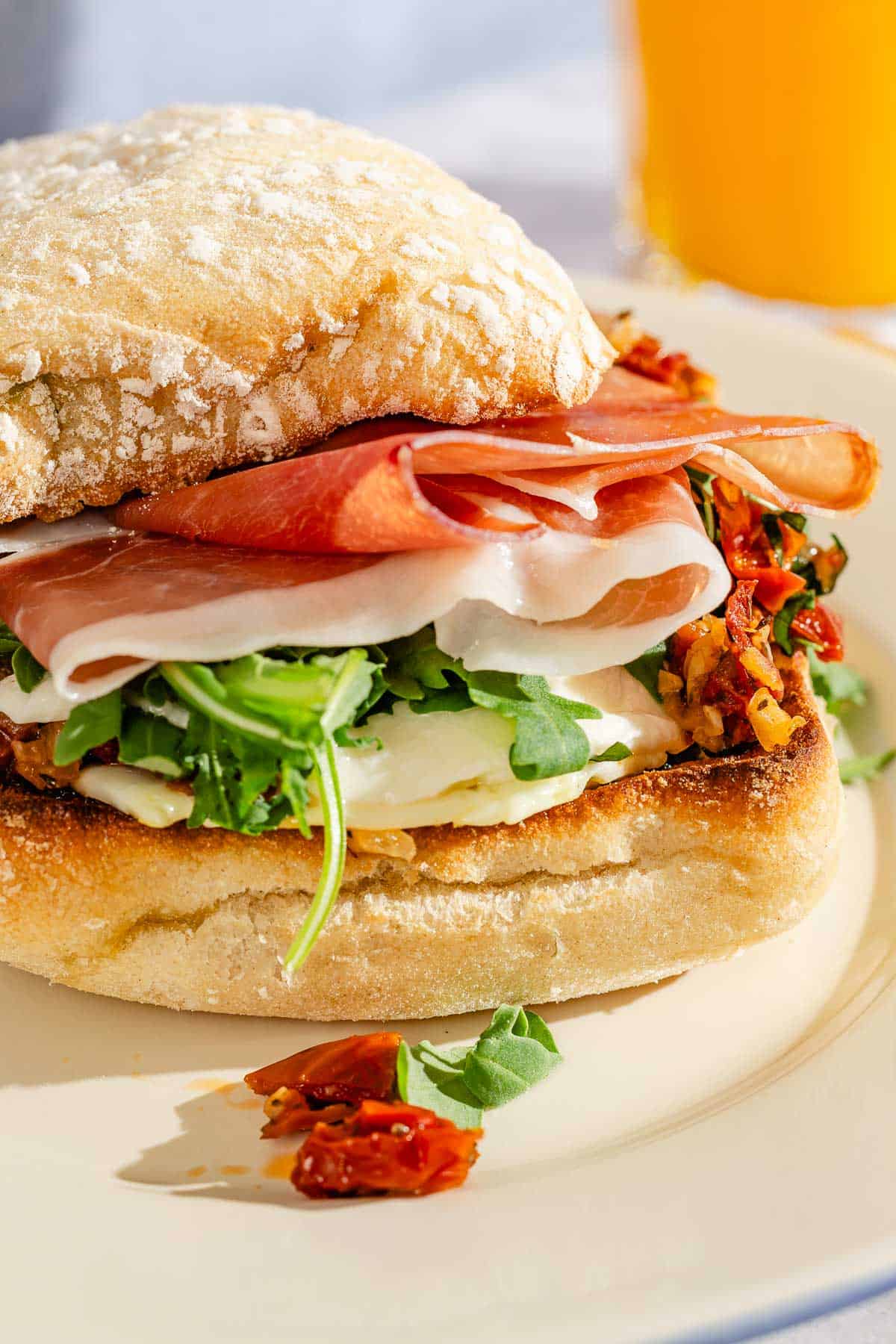 A breakfast sandwich on a plate next to a glass of orange juice.