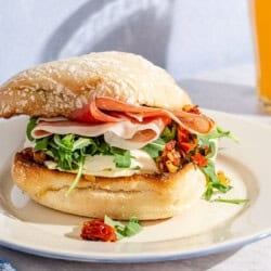 A breakfast sandwich on a plate next to a glass of orange juice.