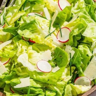Butter lettuce salad in a serving bowl with serving utensils.