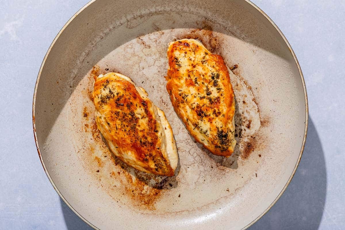2 chicken breasts being cooked in a skillet.