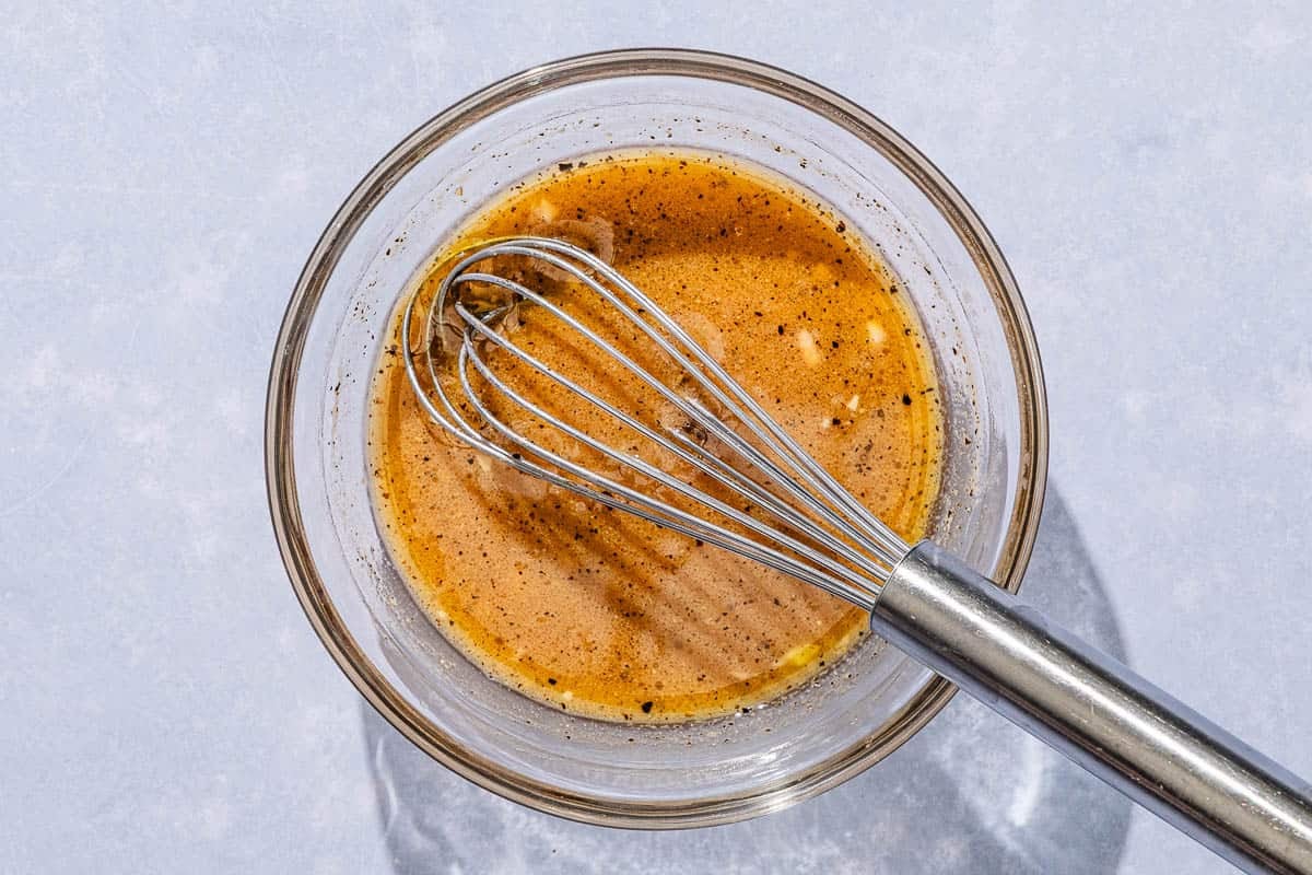 The dressing for the chicken pasta salad in a bowl with a whisk.