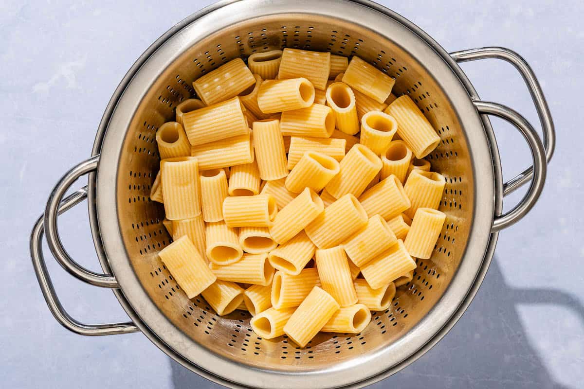 Cooked rigatoni draining in a strainer over a pot.