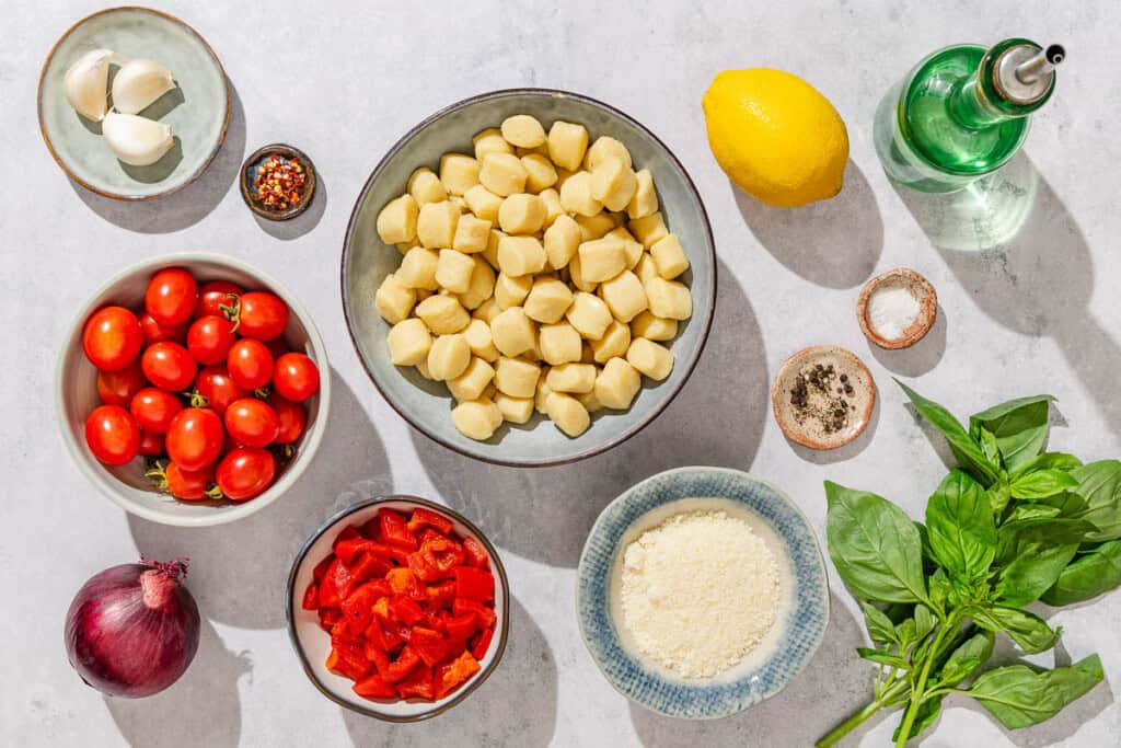Ingredients for crispy gnocchi including gnocchi, olive oil, cherry tomatoes, roasted red peppers, red onion, garlic, lemon, salt, black pepper, red pepper flakes, basil, and grated Parmigiano-Reggiano cheese