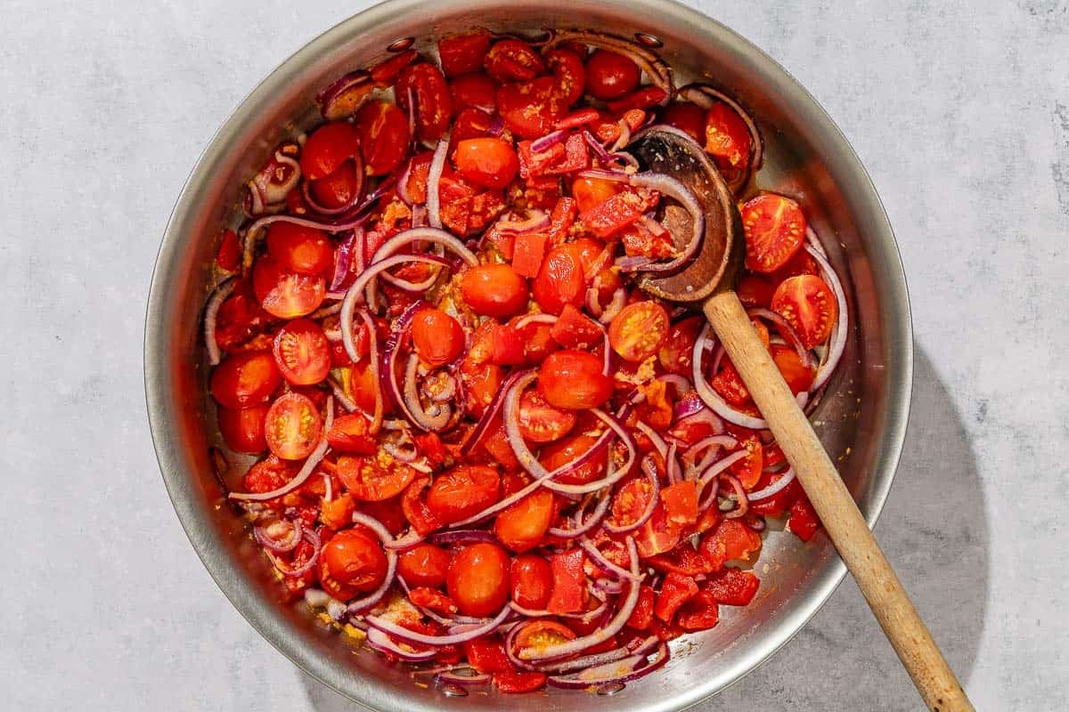 The vegetables for the crispy gnocchi being sauteed in a tall sided skillet with a wooden spoon.