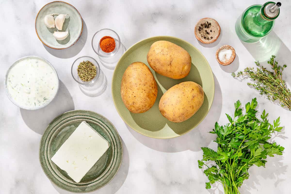 Ingredients for greek fries including russet potatoes, salt, black pepper, olive oil, garlic, fresh thyme, dried oregano, cayenne, feta cheese and fresh parsley.
