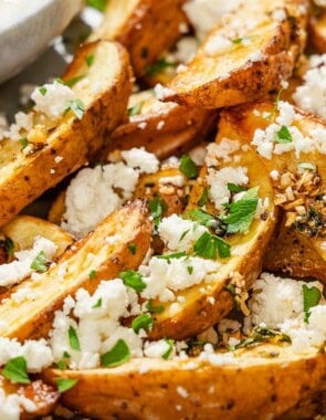 A close up of Greek fries topped with parsley and crumbled feta on a platter.