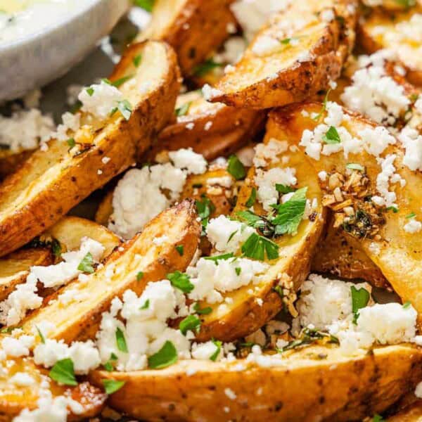 A close up of Greek fries topped with parsley and crumbled feta on a platter.