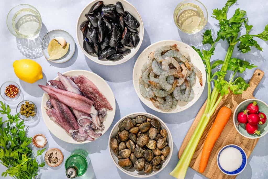 Ingredients for seafood salad including clams, white wine, seafood stock, vegetable broth, mussels, shrimp, calamari, salt, lemon, garlic, parsley, crushed red pepper, olive oil, capers, celery, carrot, radishes, water, white wine vinegar, and sugar.