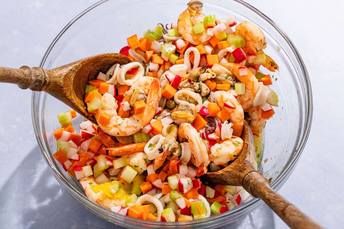The seafood salad being mixed together in a mixing bowl with wooden utensils.