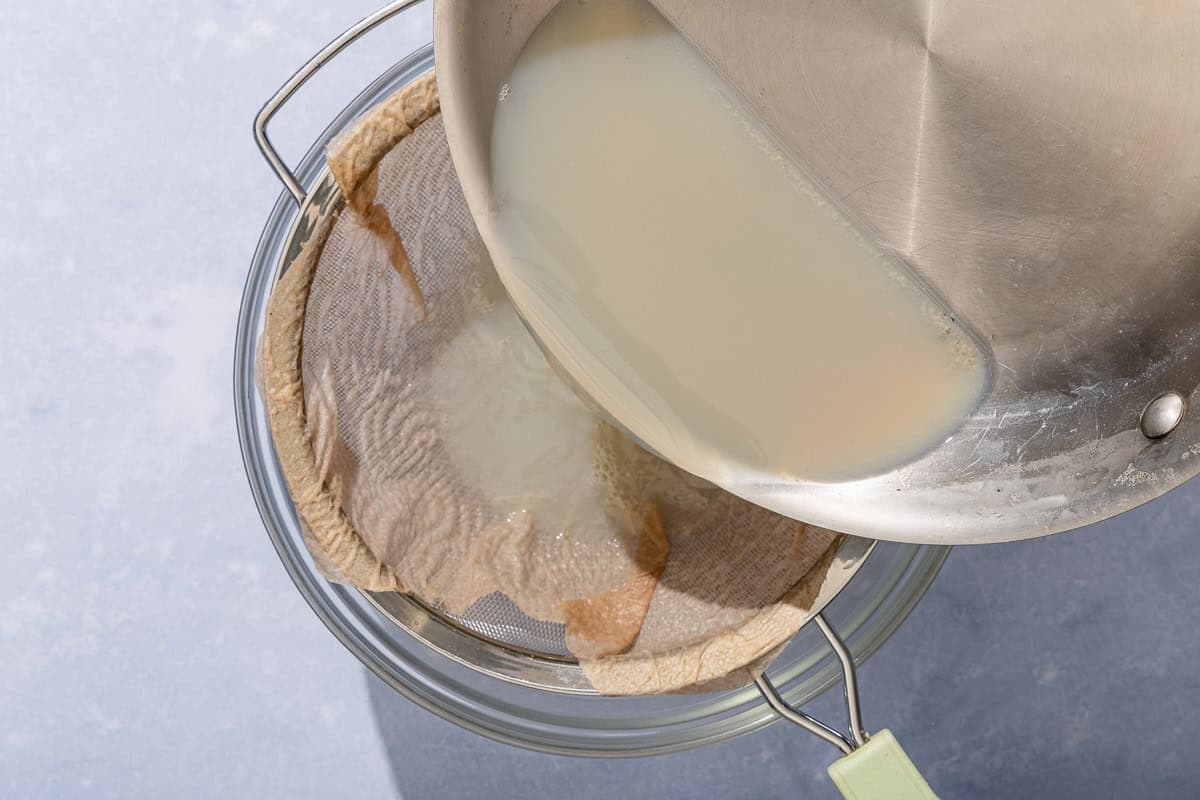 The shellfish juices for the seafood salad being drained through a fine-mesh sieve lined with a layer of damp paper towels set over a bowl.