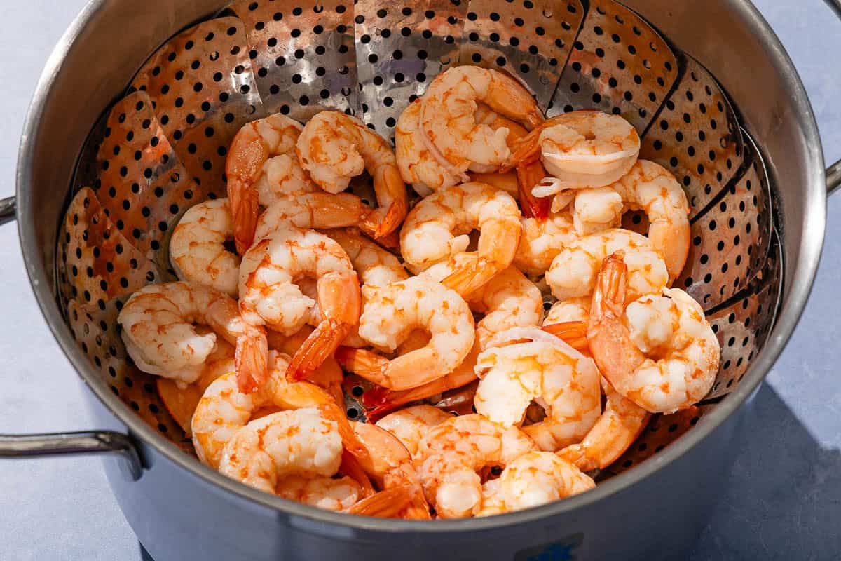 The cooked shrimp for the seafood salad in a steamer basket in a saucepan.