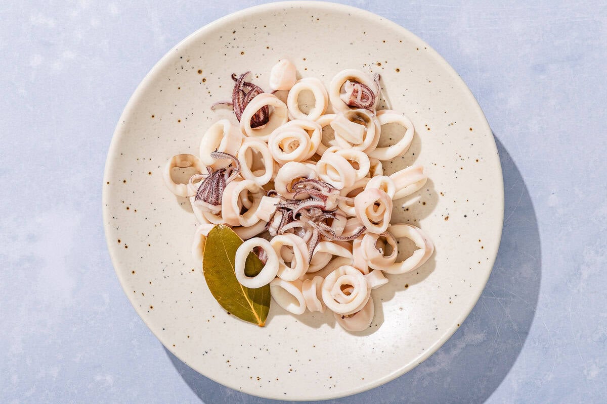 The poached calamari for the seafood salad on a plate with a bay leaf.