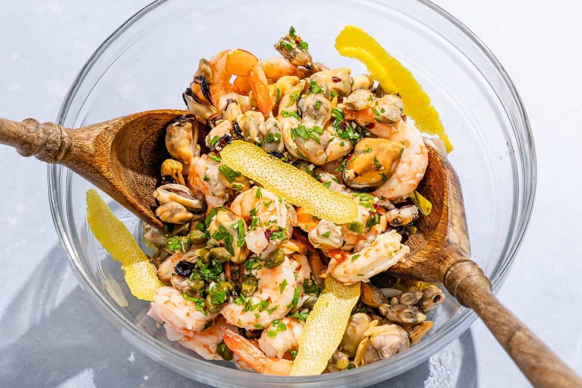 The ingredients for the seafood salad being mixed together in a bowl with wooden serving utensils.