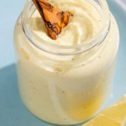 A jar of lemon pesto with a wooden spoon resting on a plate with a lemon slice.