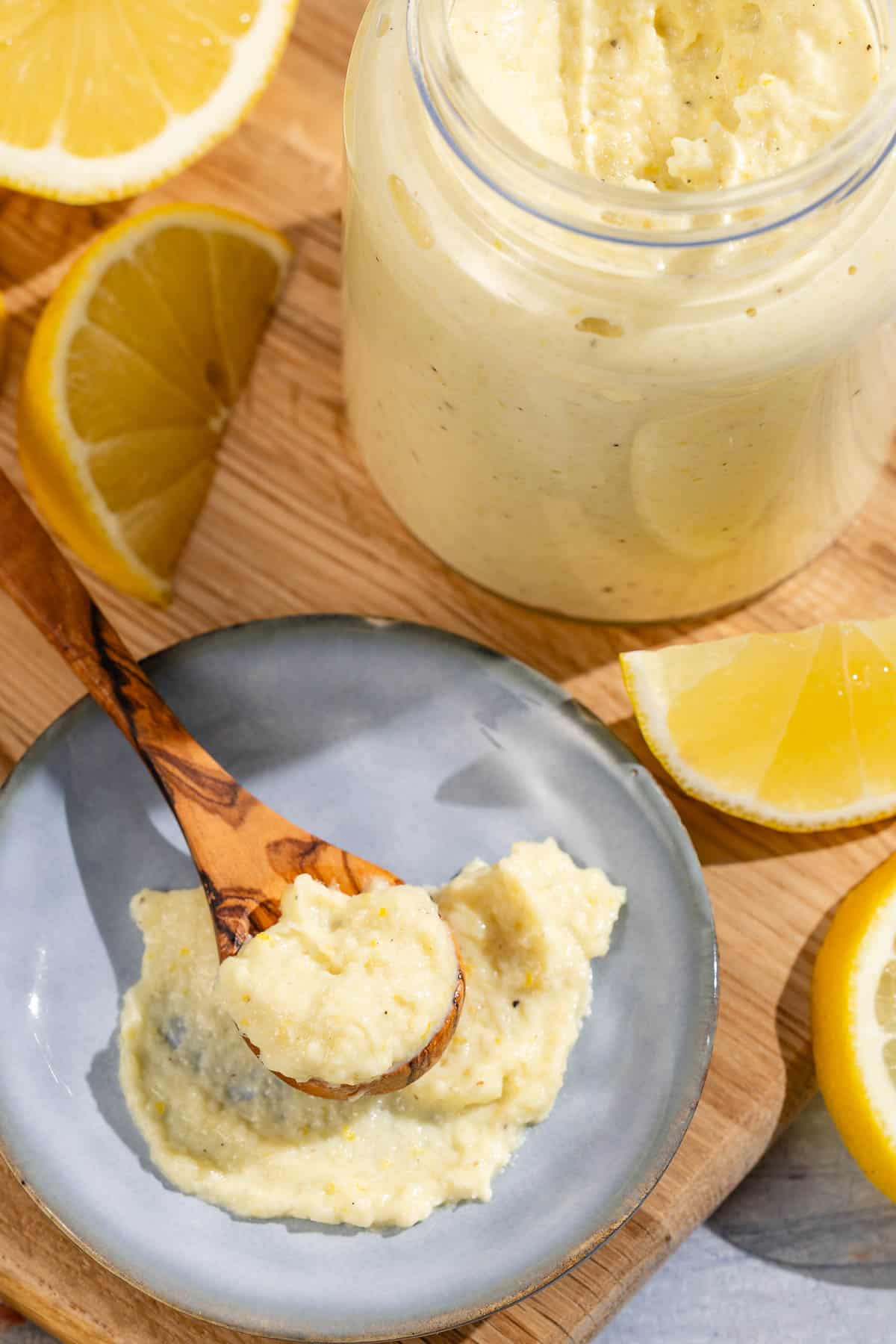 A spoonful of lemon pesto on a plate sitting on a wooden cutting board. Next to this is a jar of lemon pesto and lemon slices.