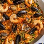 Paella in a paella pan next to a kitchen towel and a bowl of lemon wedges.