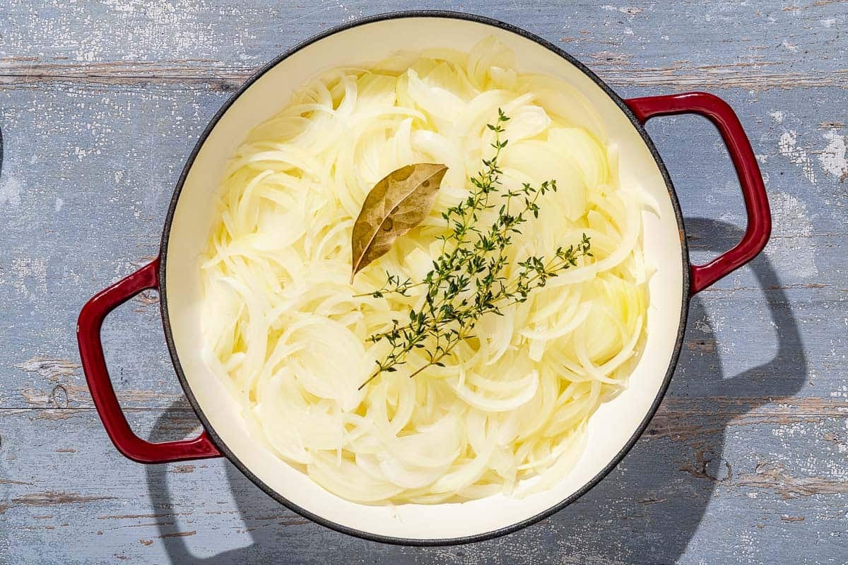 The sliced onions for the pissaladière topped with thyme and a bay leaf being carmelized in a skillet.
